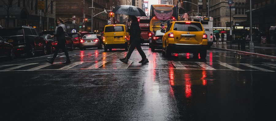 Pedestrians crossing a rain-soaked Midtown street between yellow taxis